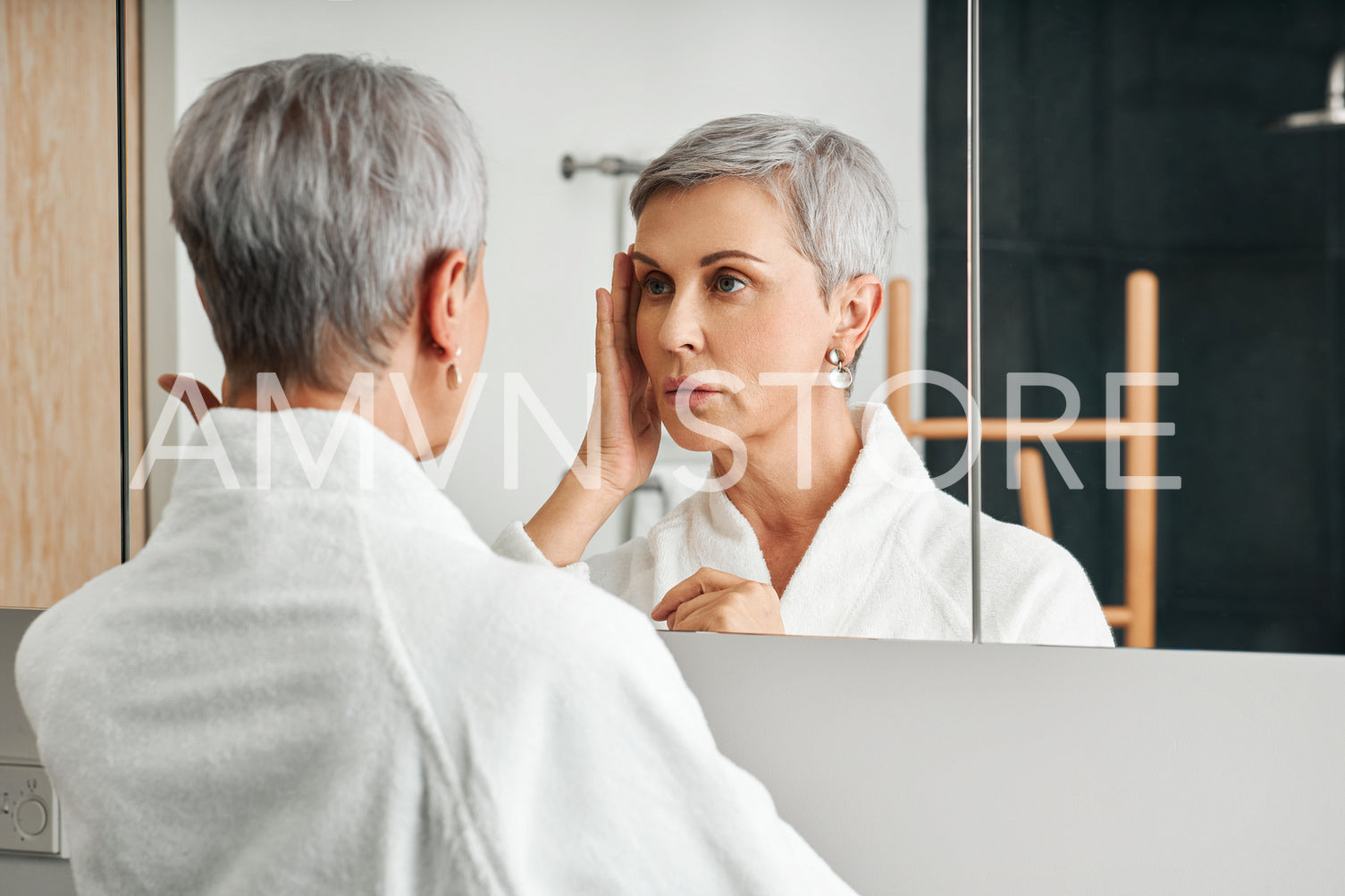 Senior female touching her face in a bathroom. Mature woman inspecting face in the morning.