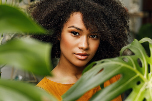 Portrait of a young woman. Beautiful female posing in plant shop near monstera leaves.