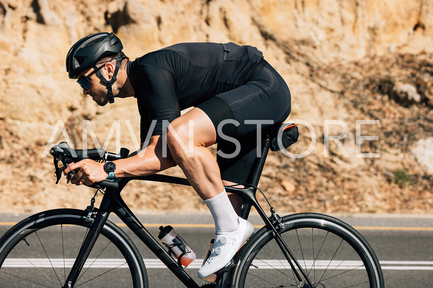 Professional cyclist in black sportswear riding road bike against the mountain. Muscular male doing intense training on bike outdoors.