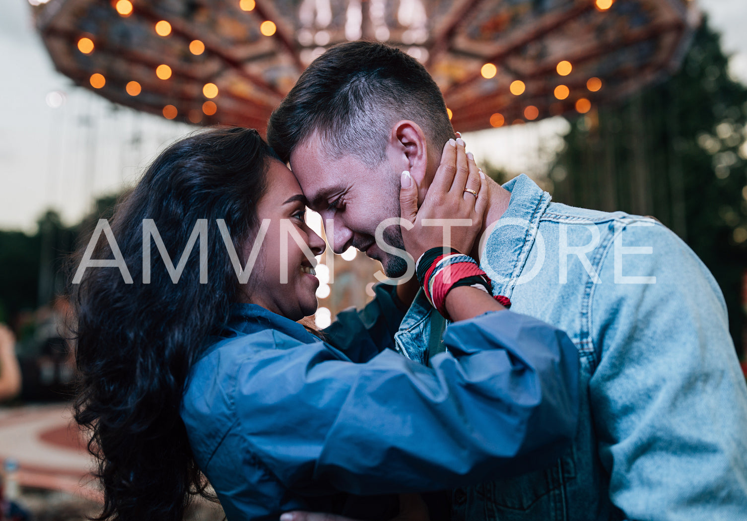 Smiling couple embracing at night against carousel in an amusement park