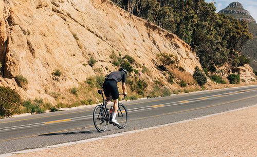 Rear view of a professional cyclist riding up on an empty road. Young male in cycling attire on a road bike.