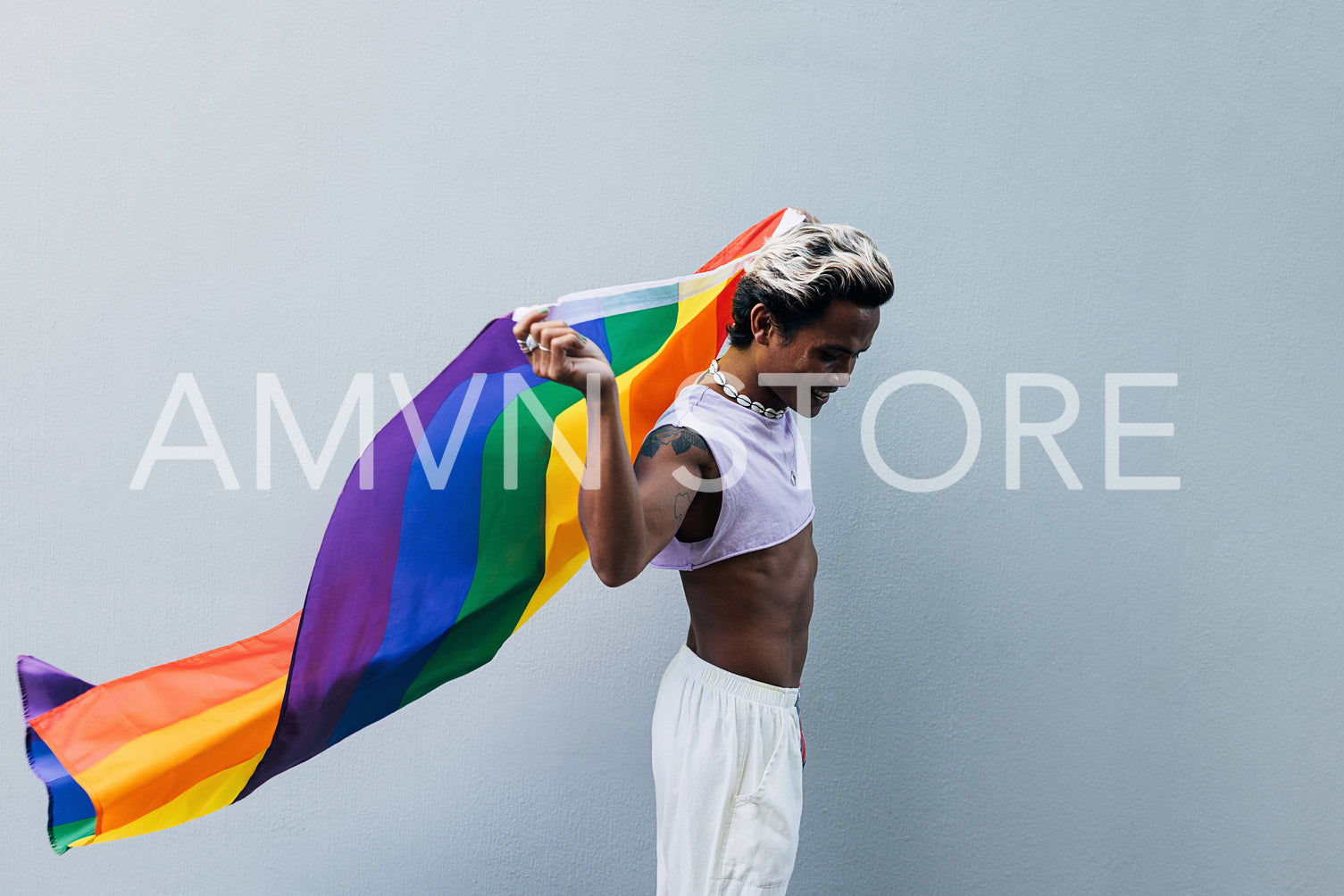 Side view of a young stylish man in stylish clothes walking with rainbow LGBT flag