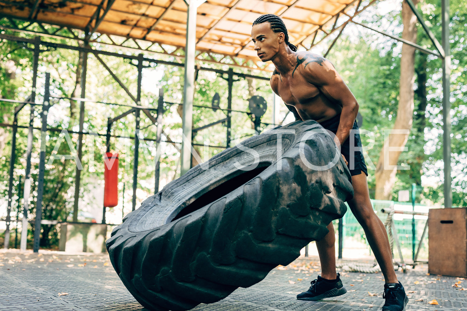 Muscular man exercising with heavy tire on sports ground outdoors	