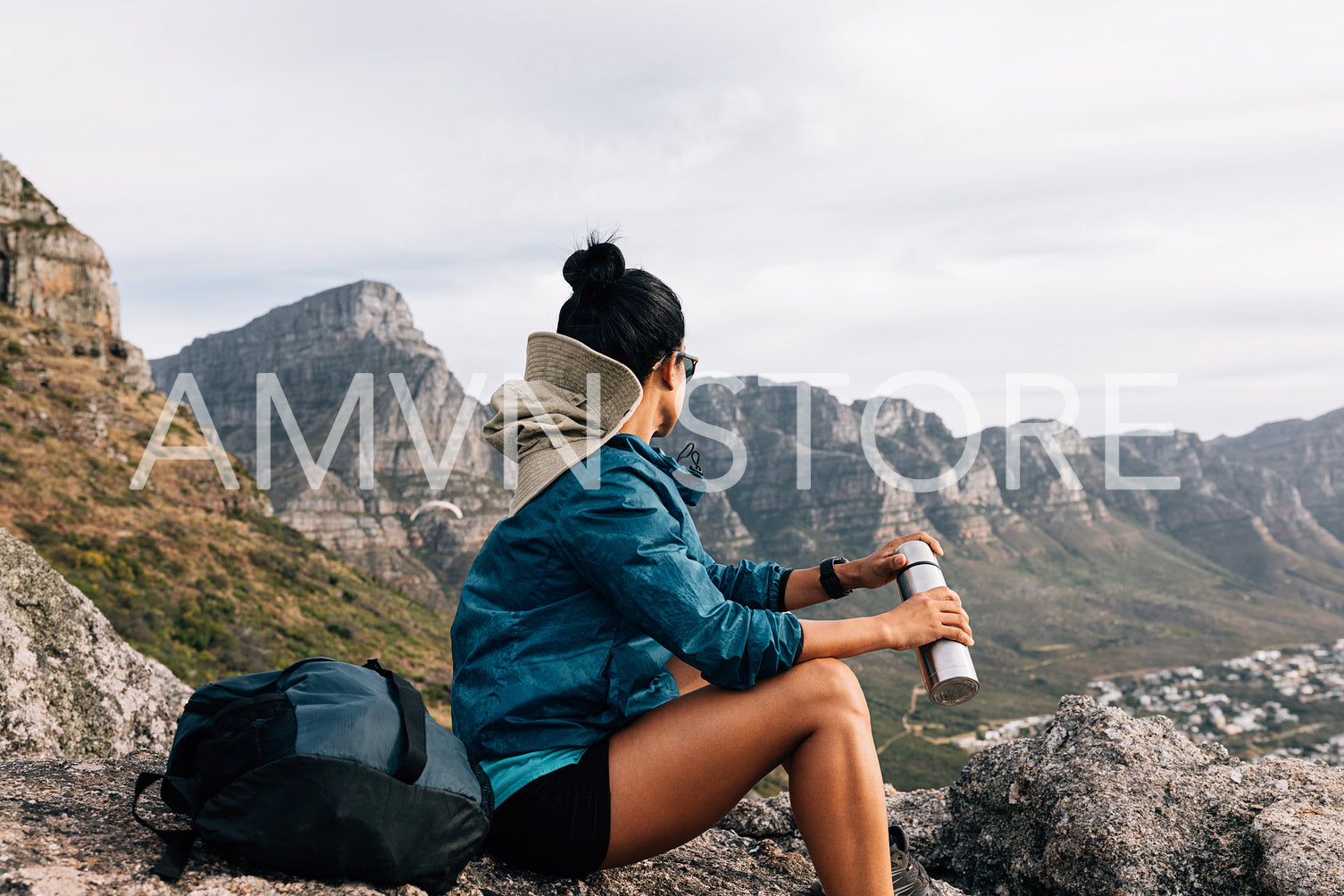 Female mountain climber looking at the view while sitting on a rock, holding a thermos