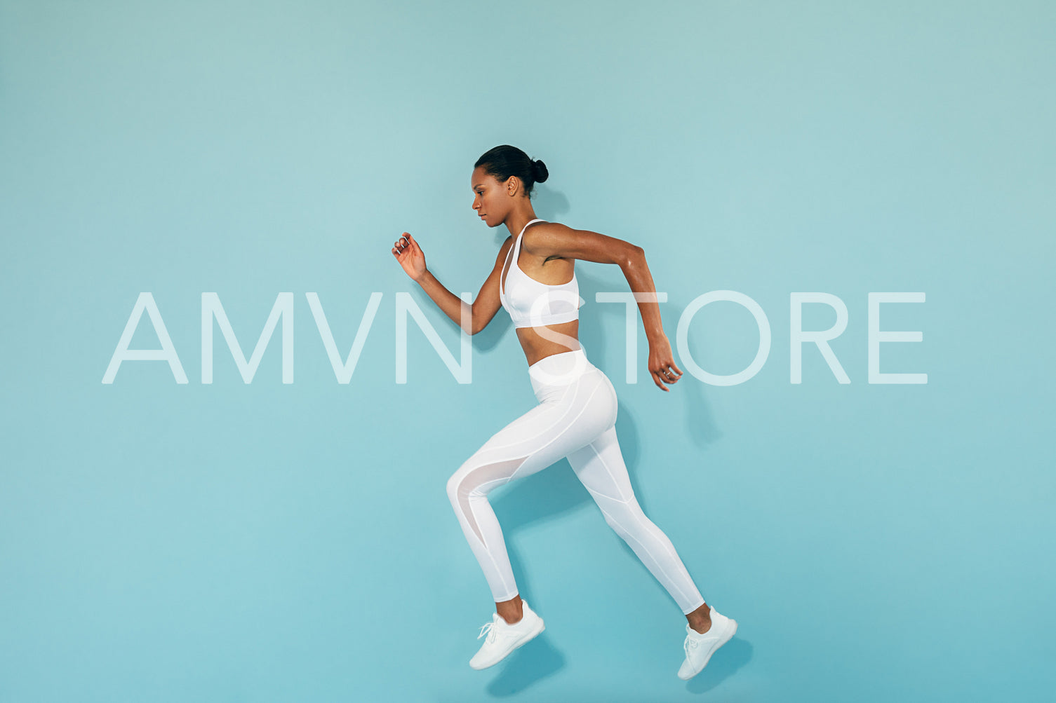 Side view of a woman running and jumping over blue background in studio	