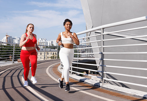 Two females in sportswear with different color running on bridge at sunny day