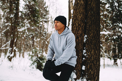 Young sportsman resting during workout, leaning on a tree