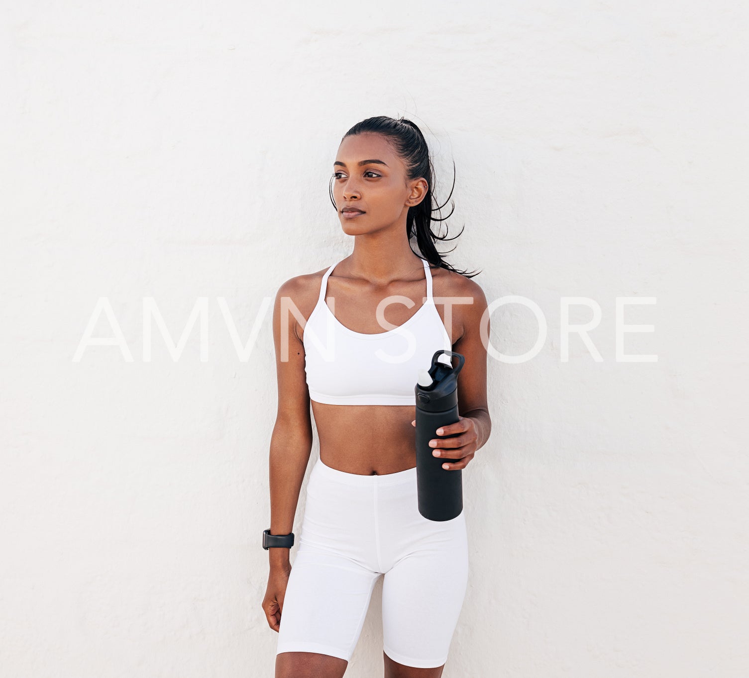 Confident fitness female athlete with bottle relaxing at a white wall