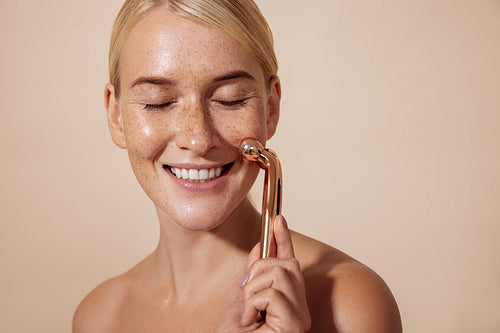 Happy woman using facial roller. Young female doing skincare routine.