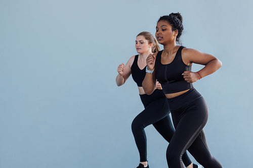 Two females competing each other while running outdoors. Young women jogging outdoors wearing black sportswear.