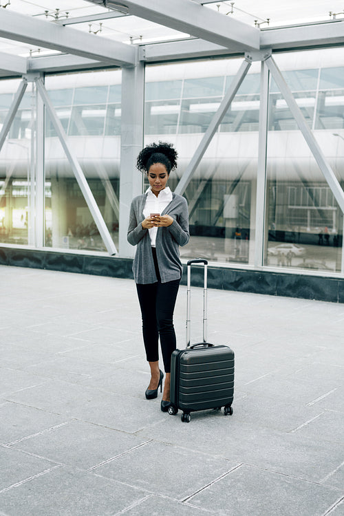 Front view of young businesswoman standing with baggage at airport