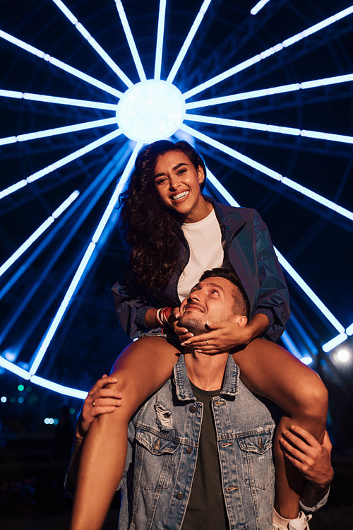 Young woman looking at camera against lights of ferris wheel. Couple at night during the festival.