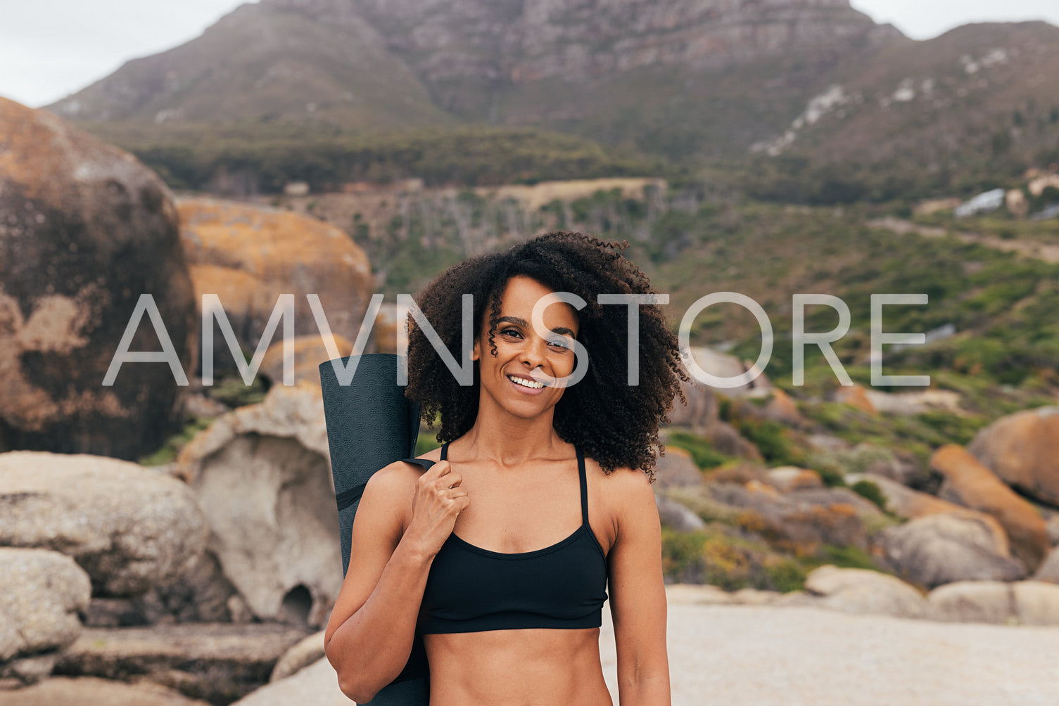 Portrait of a woman with curly hair with yoga mat standing outdoors by mountains