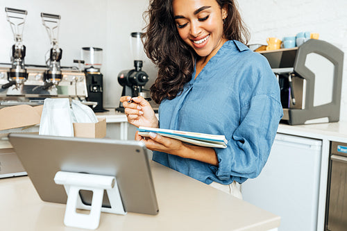 Smiling woman holding a note book in coffee shop. Cafe owner standing at table.