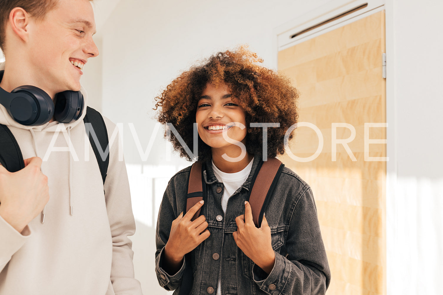 Two cheerful classmates standing together in corridor