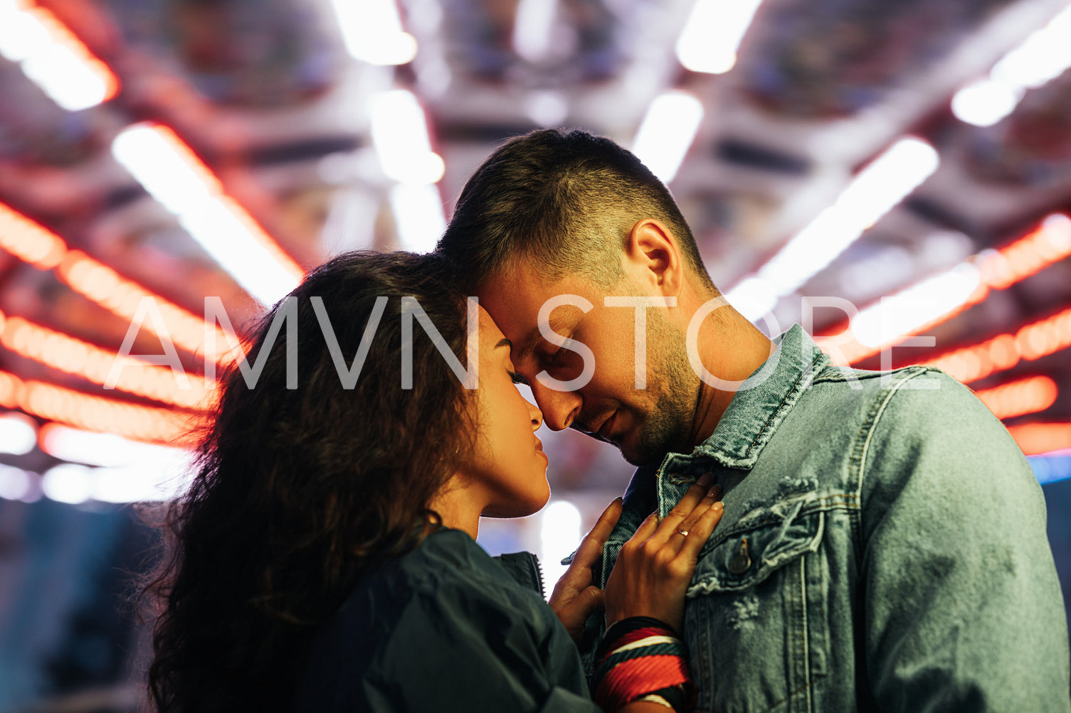 Boyfriend and girlfriend standing together head to head with closed eyes against night lights in an amusement park