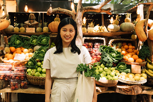 Portrait of an Asian woman standing on an outdoor market. Female with a shopping bag standing at a stall with organic food.