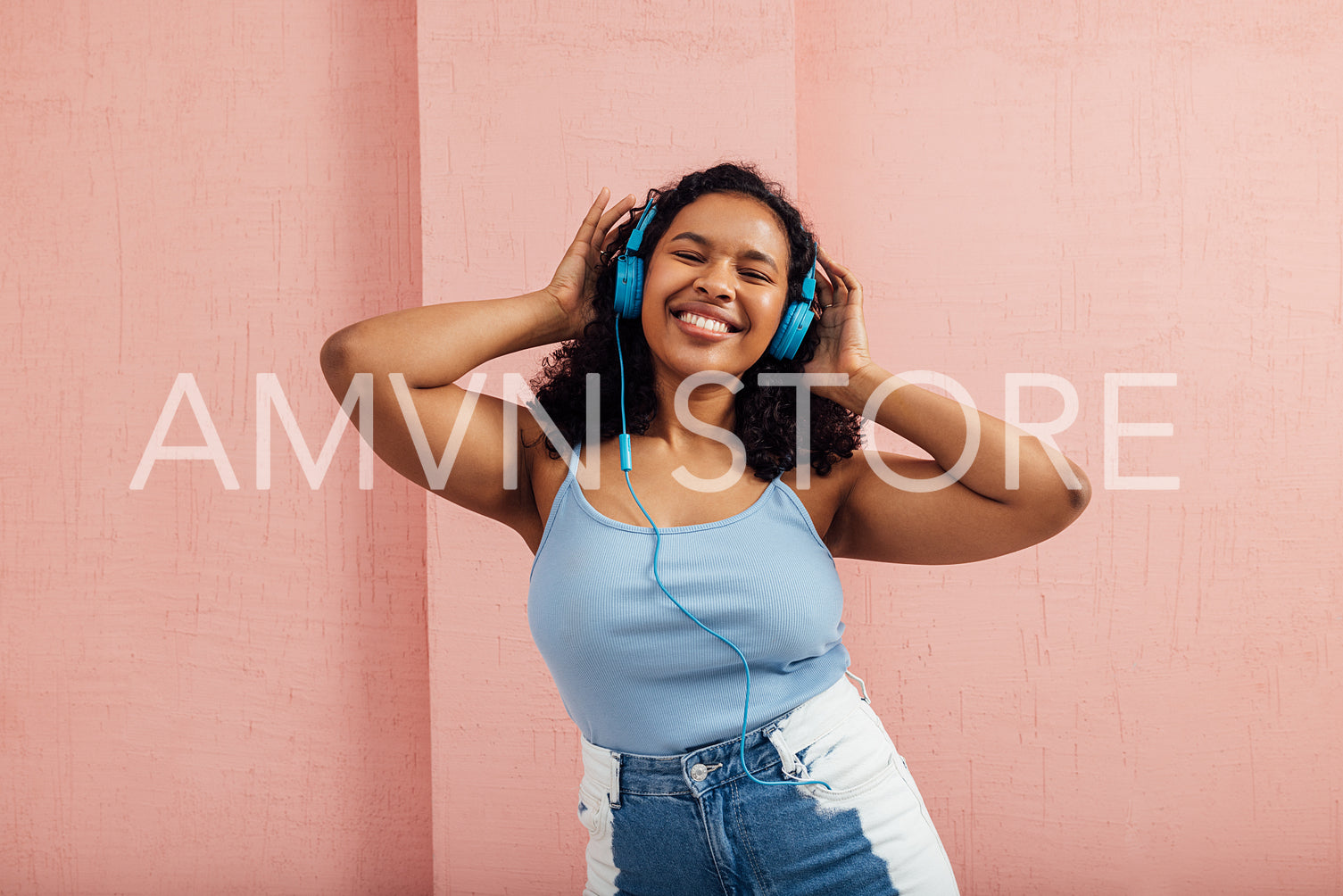 Happy woman with curly hair enjoying music listening by blue headphones