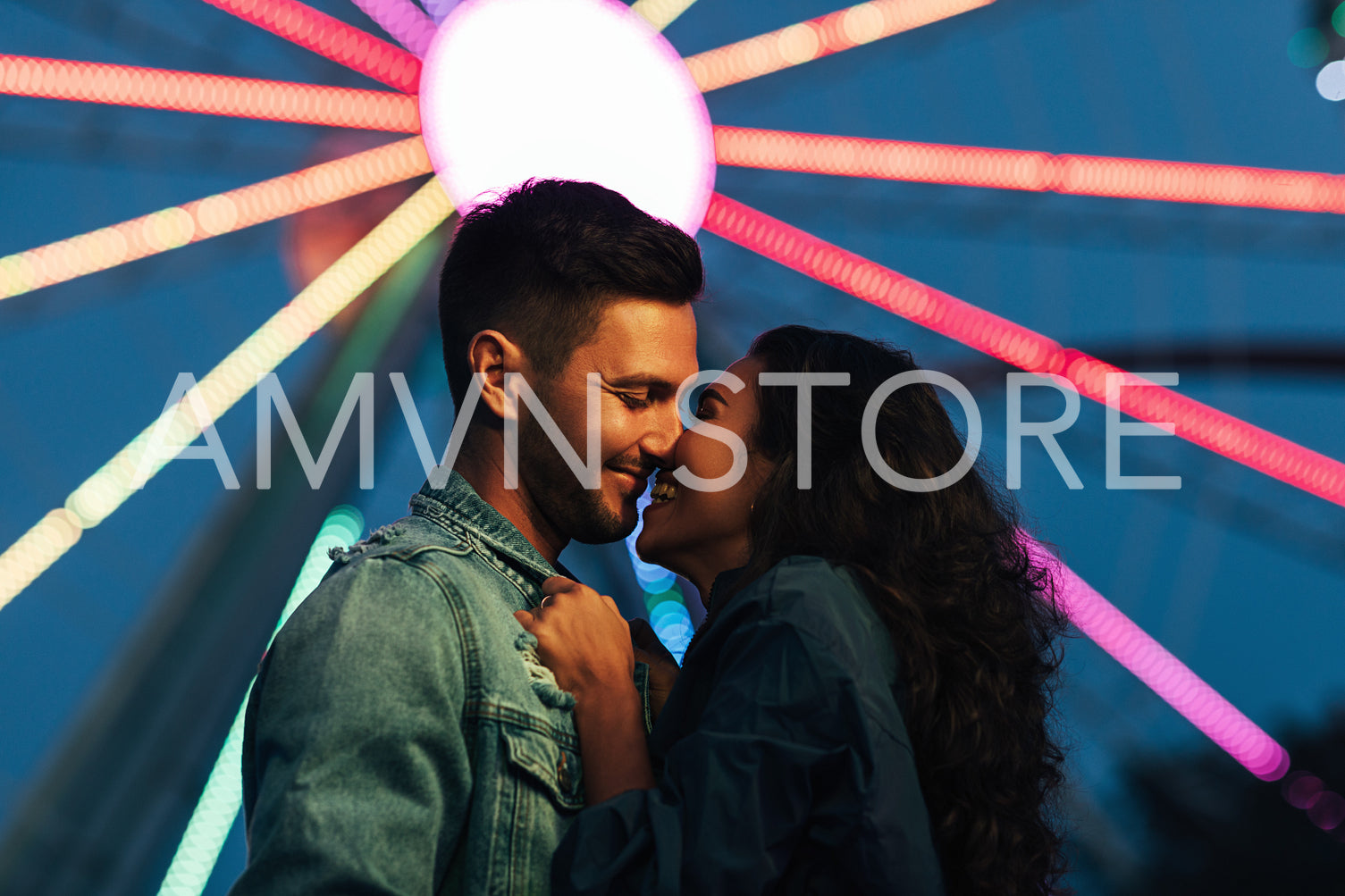 Side view of young happy couple against Ferris wheel at night