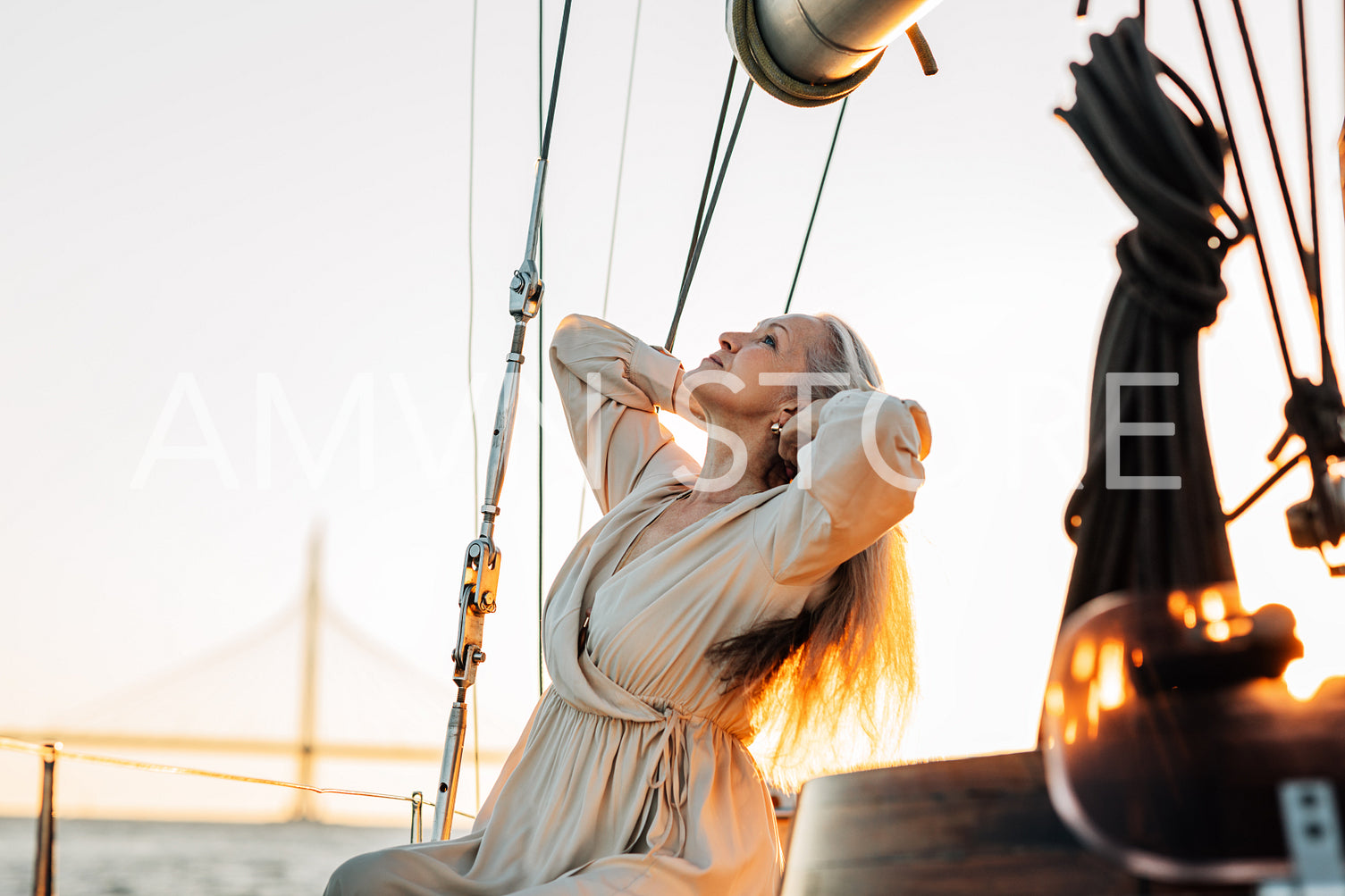 Side view of elegant senior woman sitting on a yacht deck and adjusting her long hair at sunset	