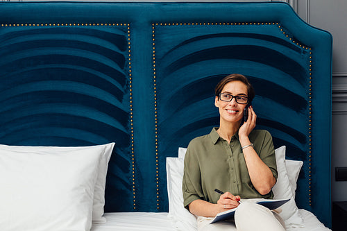 Mid adult woman lying on a bed in hotel room talking on mobile phone and looking away