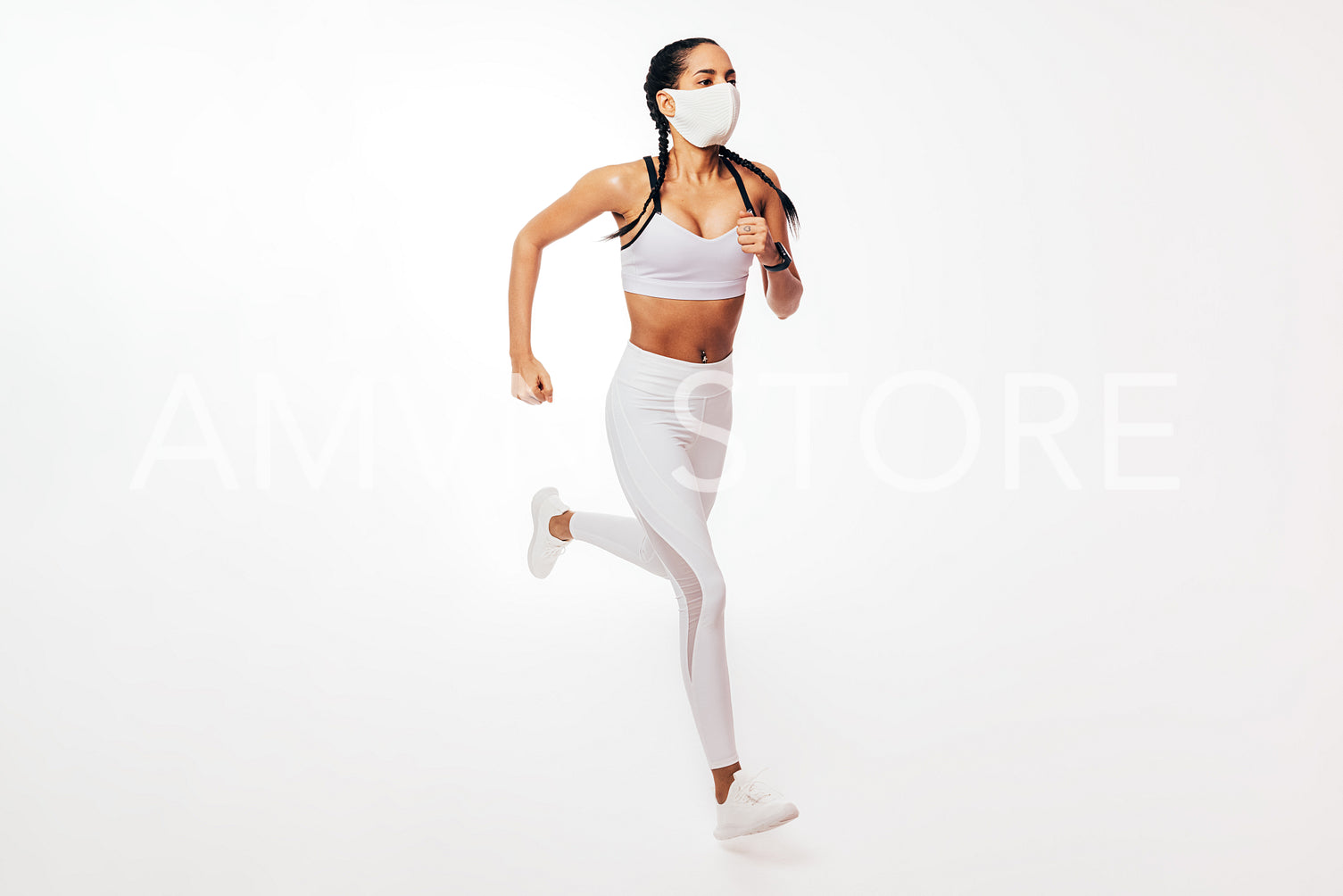 Young fit woman in face mask running on white background in studio