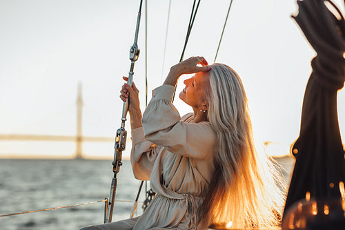 Side view of a mature woman sitting on a yacht and adjusting her hair at sunset