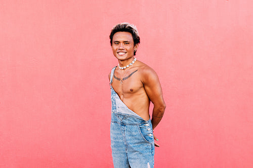 Portrait of a smiling handsome guy in casuals standing at pink w