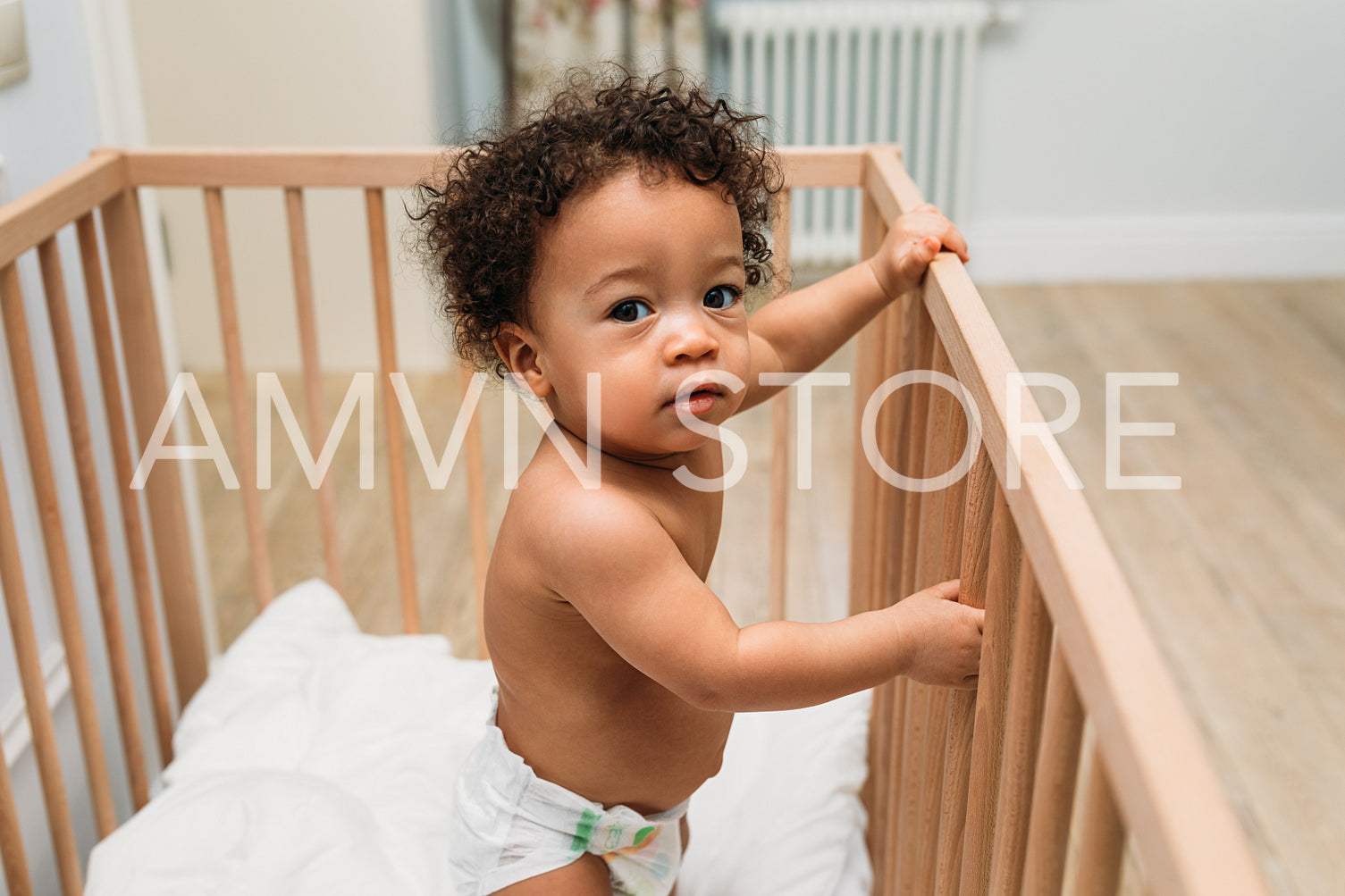 Portrait of curly haired toddler standing in a crib, looking at camera	