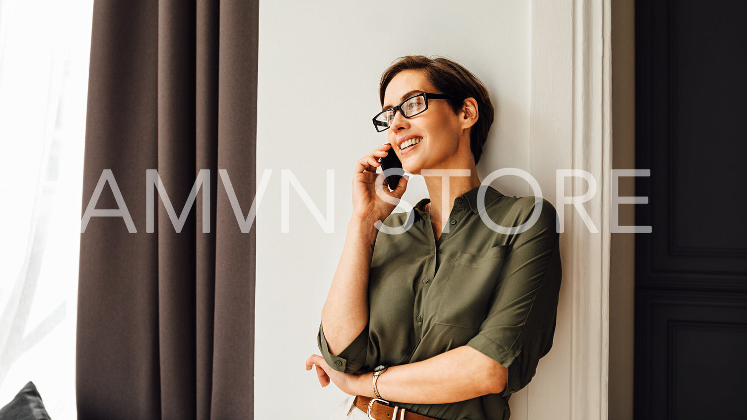 Beautiful businesswoman talking on a mobile phone while looking at window in hotel room	