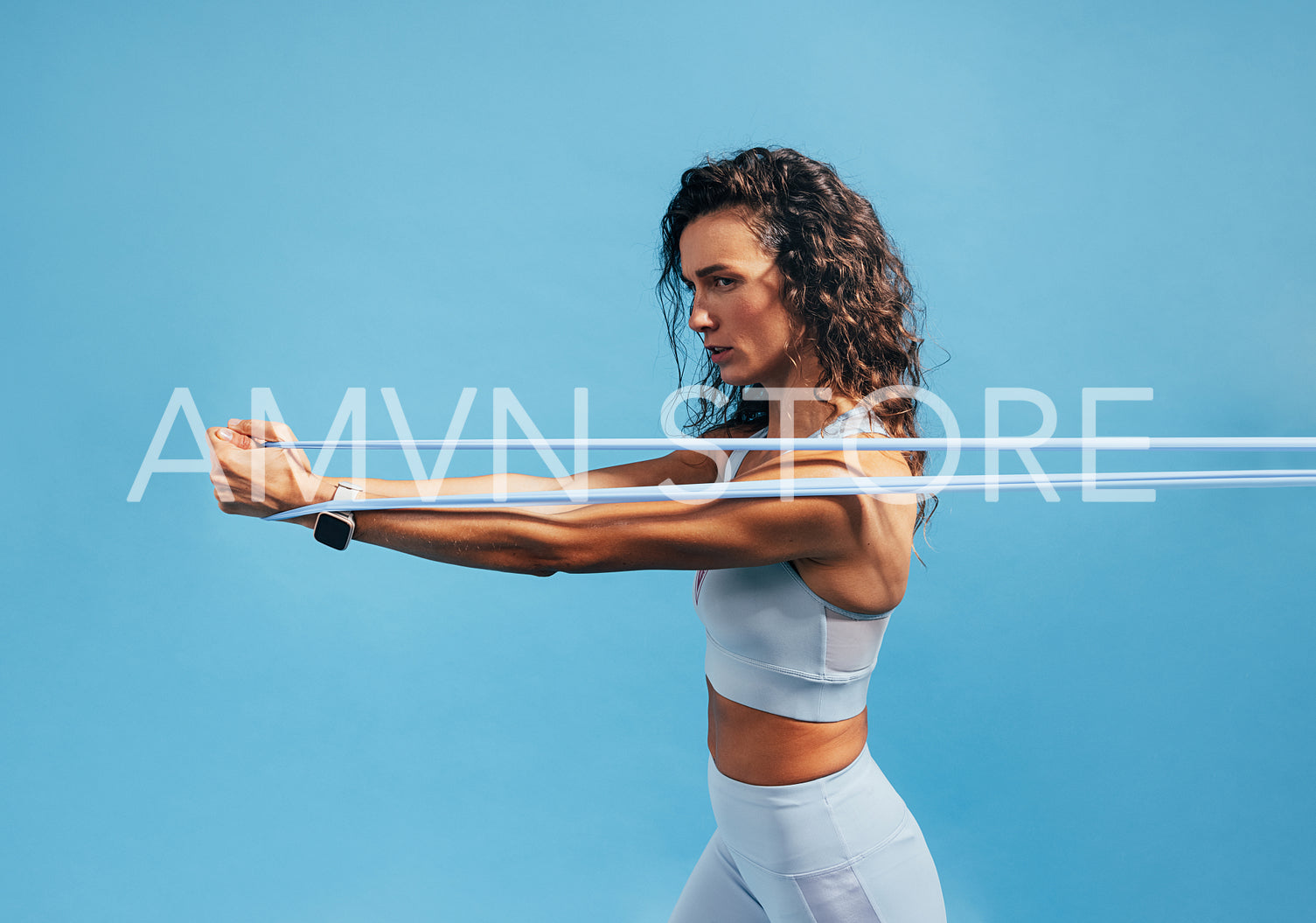 Side view of young fit woman doing intense training with resistance band on blue background