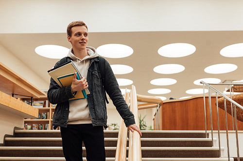 Male university student with books in library looking away