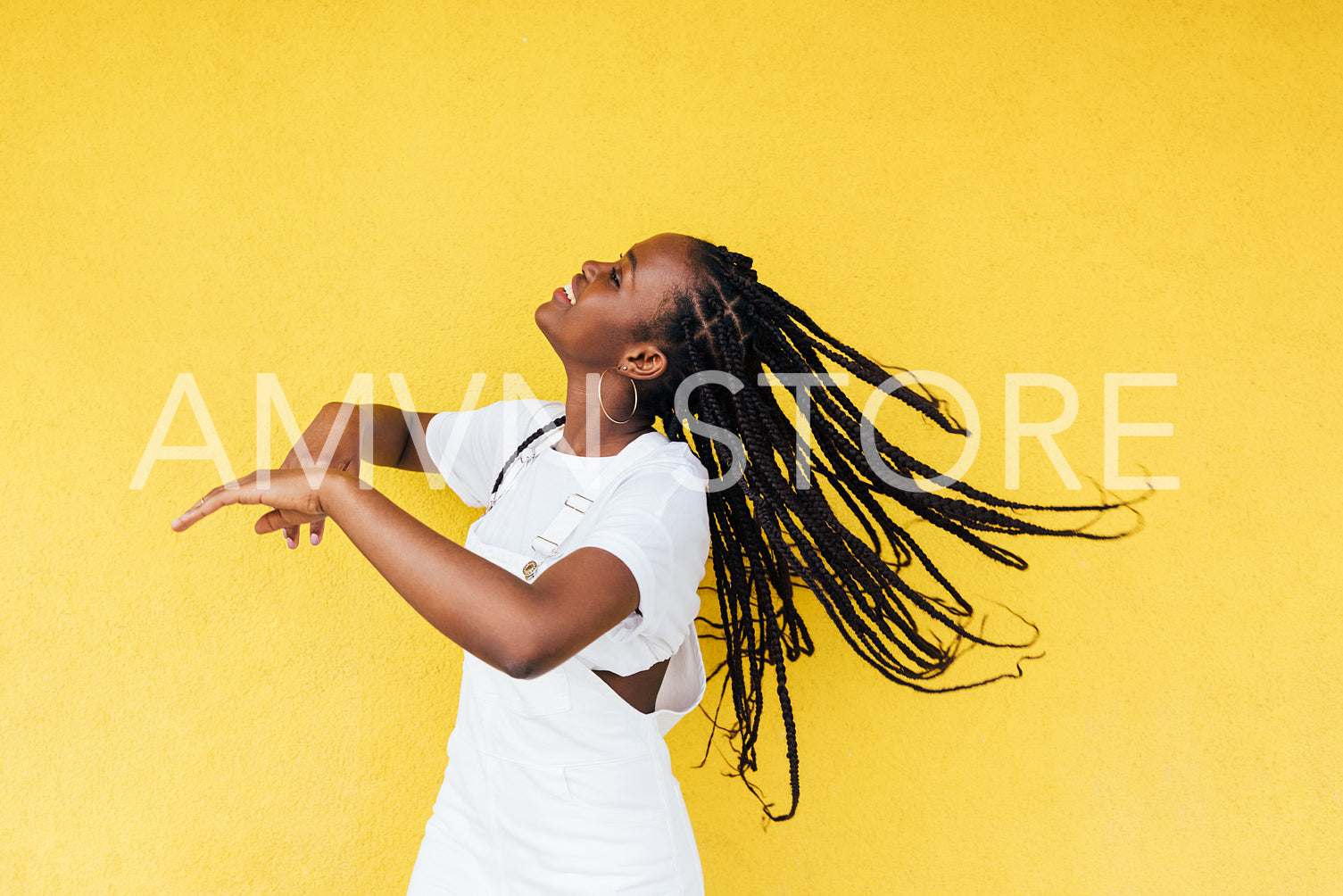 Side view of young happy woman with long braids dancing at yellow wall outdoors