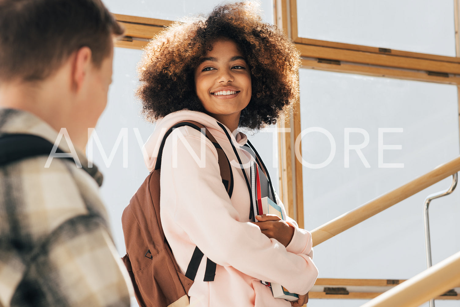 Smiling girl with books and backpack looking at classmate while walking on stairs