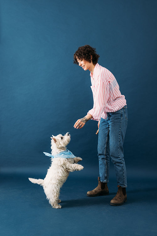 Side view of young woman in casuals standing in studio on blue b