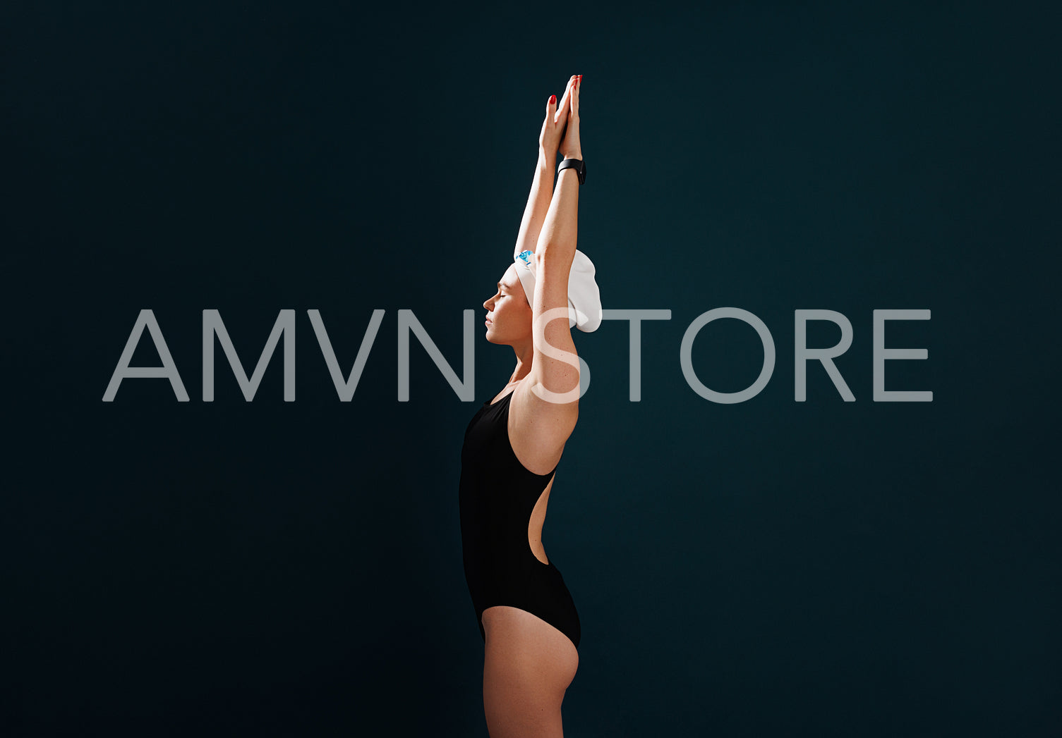 Side view of female swimmer in a swimsuit standing against a blue backdrop with raised hands