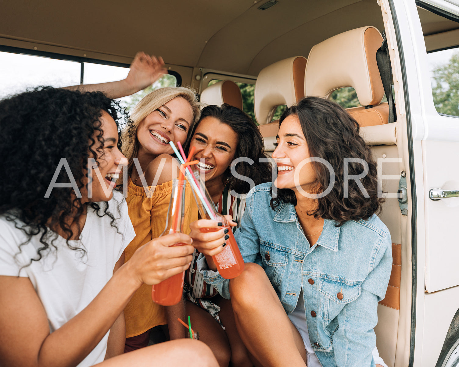 Happy women sitting together in van during road trip. Smiling females having fun and drinking cocktails in car.