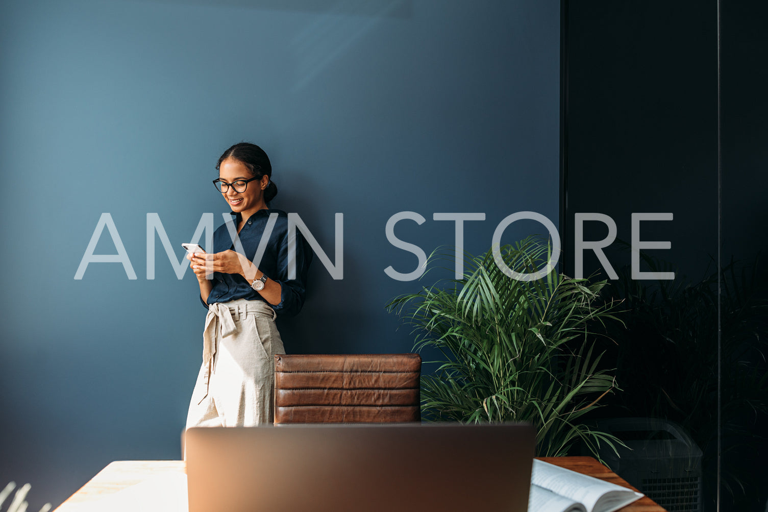 Young woman using a cell phone at a home office. Side view of a female entrepreneur working remotely.	