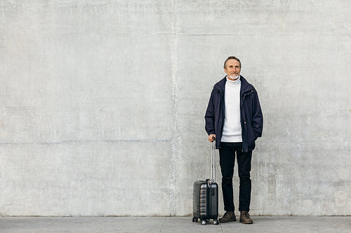 Senior tourist standing at wall with suitcase