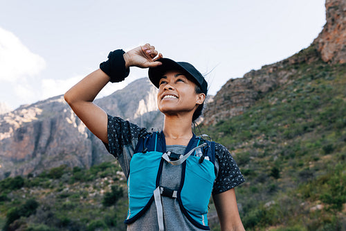 Smiling woman hiker looking up. Female in sports clothes holding cap and searching trail.