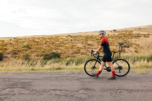 Side view of a professional female cyclist walking with bike on a country road