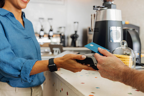 Unrecognizable female employee taking payment from customer in coffee shop. Hand of a customer making contactless payment using credit card.