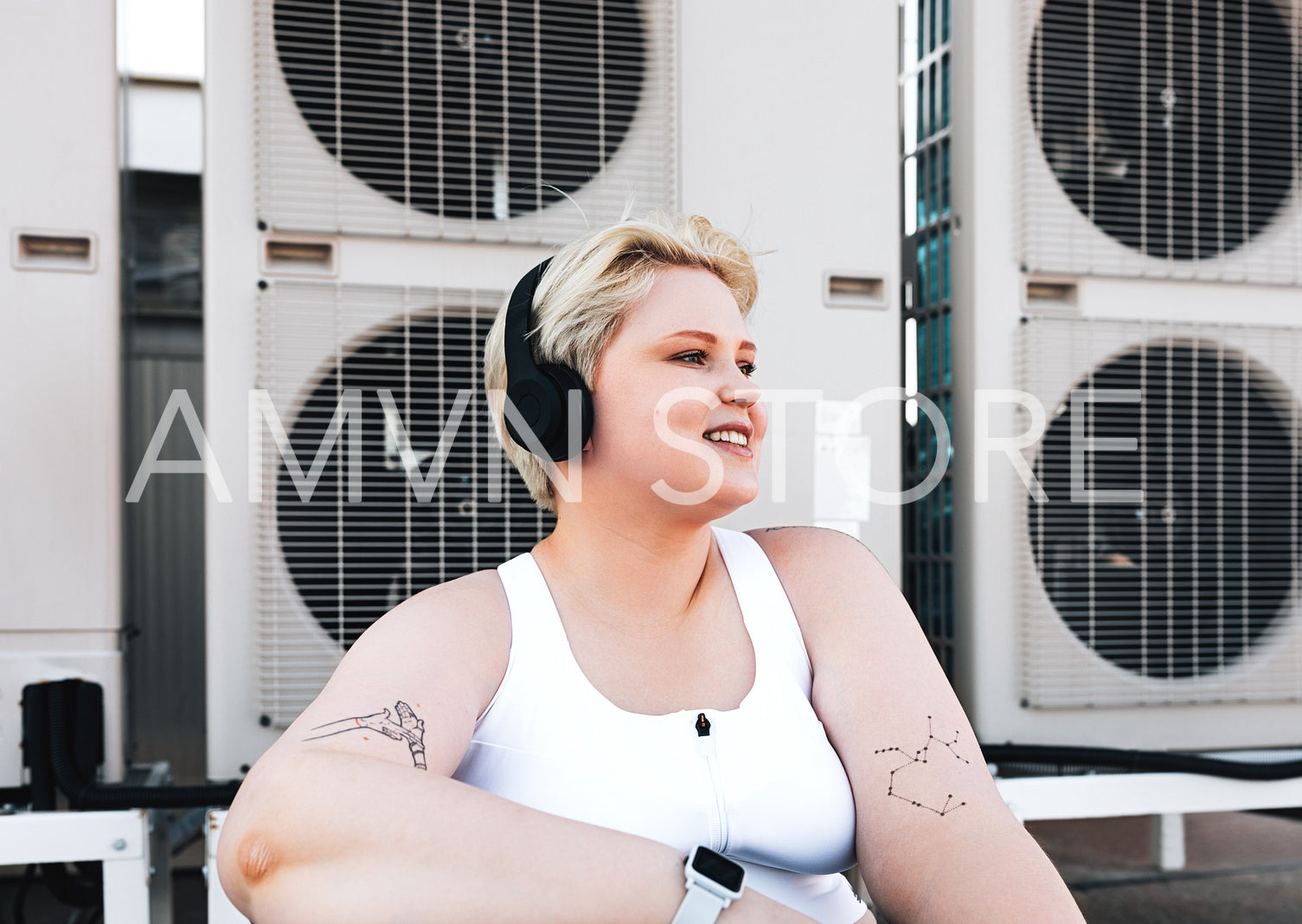 Smiling curvy woman in sportswear sitting on the roof at air conditioning units	