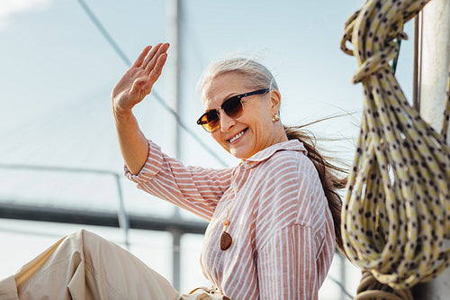 Happy woman wearing sunglasses waving her hand and looking at camera