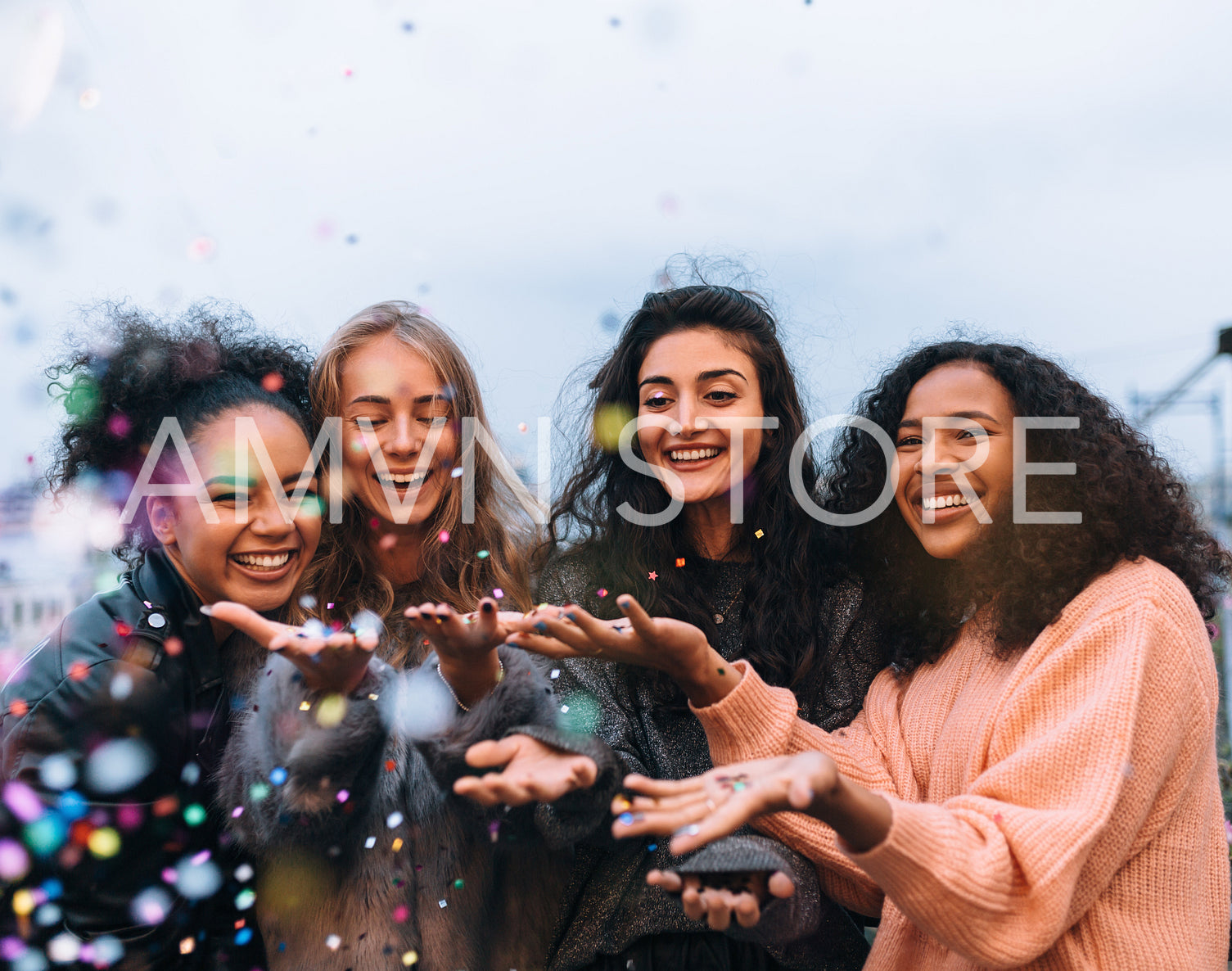 Four happy females throwing confetti outdoors in the evening