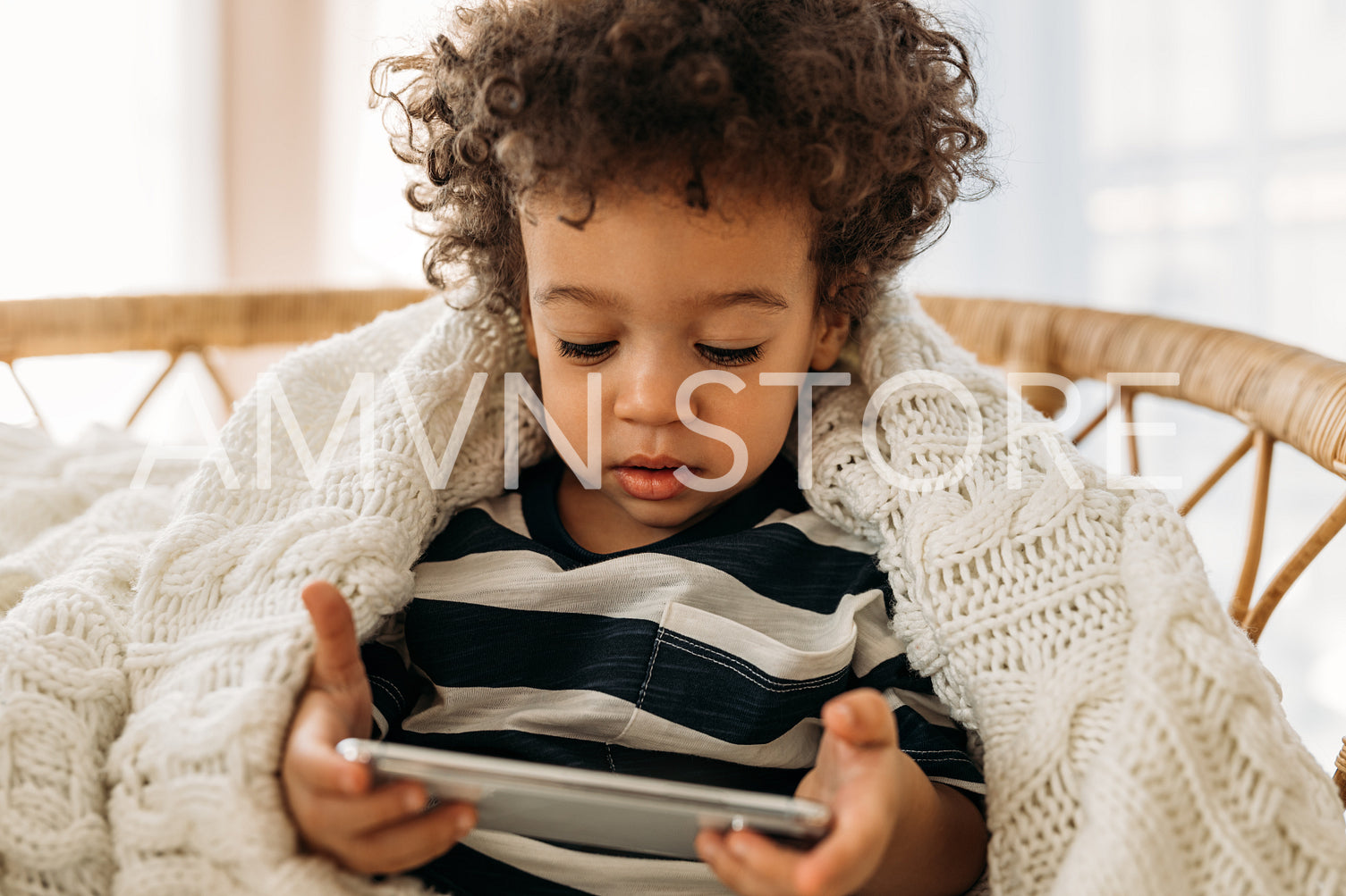 Little cute boy with curly hair sitting on an armchair under a plaid