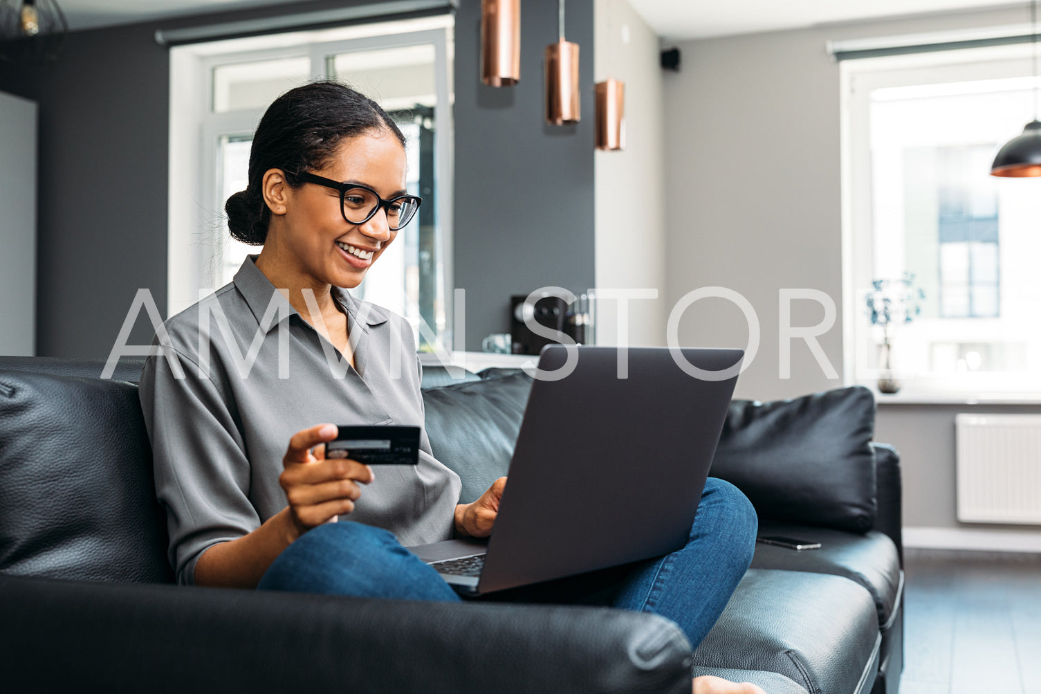 Happy woman sitting on a sofa in the living room holding a credit card with a laptop on her laps	