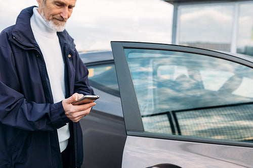 Senior man typing on cell phone while standing at rental car