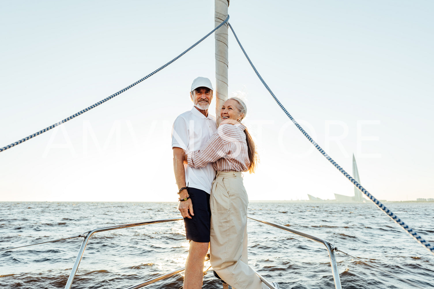 Two elderly people in casuals standing on yacht bow and smiling	