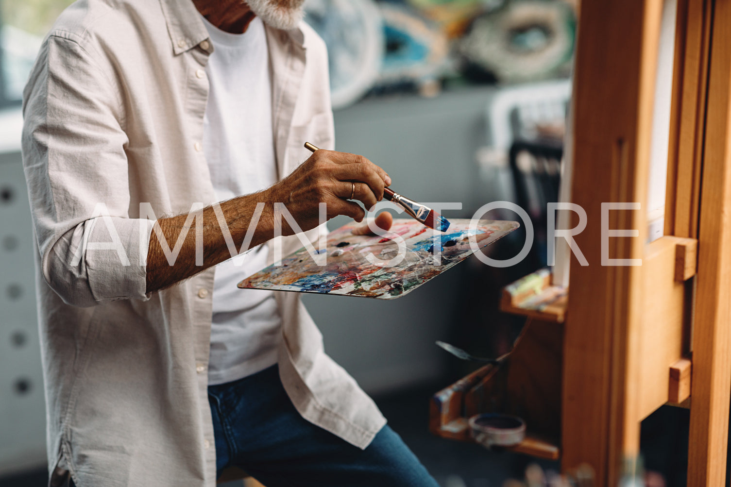 Male hand holding paintbrush and mixing oil paints on colorful messy palette	